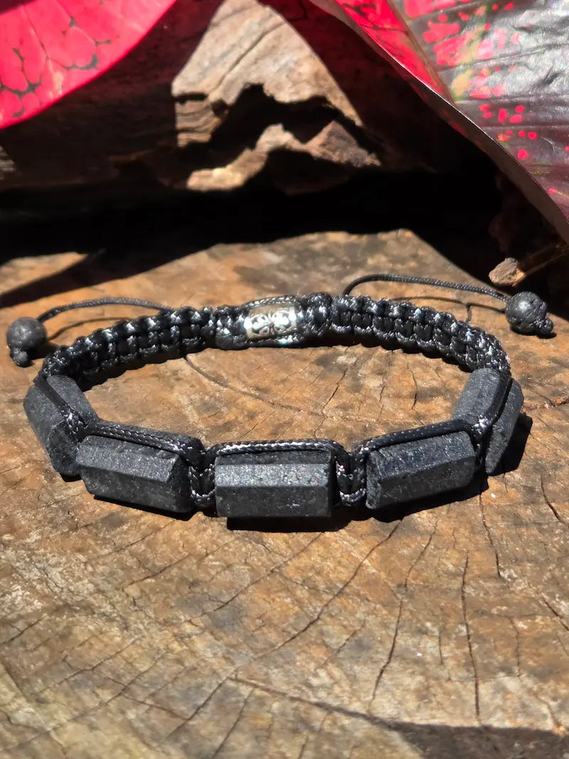 A black beaded bracelet with rectangular black Tourmaline beads and a silver-toned metal clasp, displayed on a textured wooden surface.