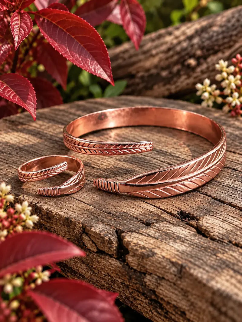 Copper bracelet with a matching ring with a feather design on a natural wooden surface with red leaves in the background