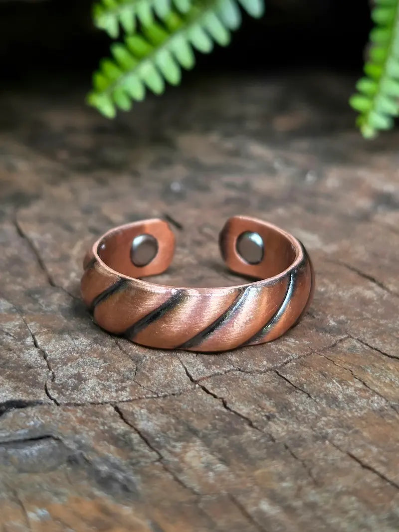 Copper ring with a twisted design on a natural wooden surface with green leaves in the background