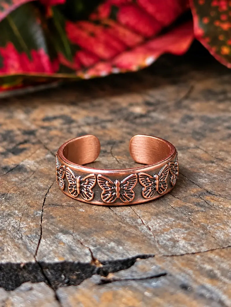 Copper ring with a butterfly design resting on a natural wooden surface with red leaves in the background