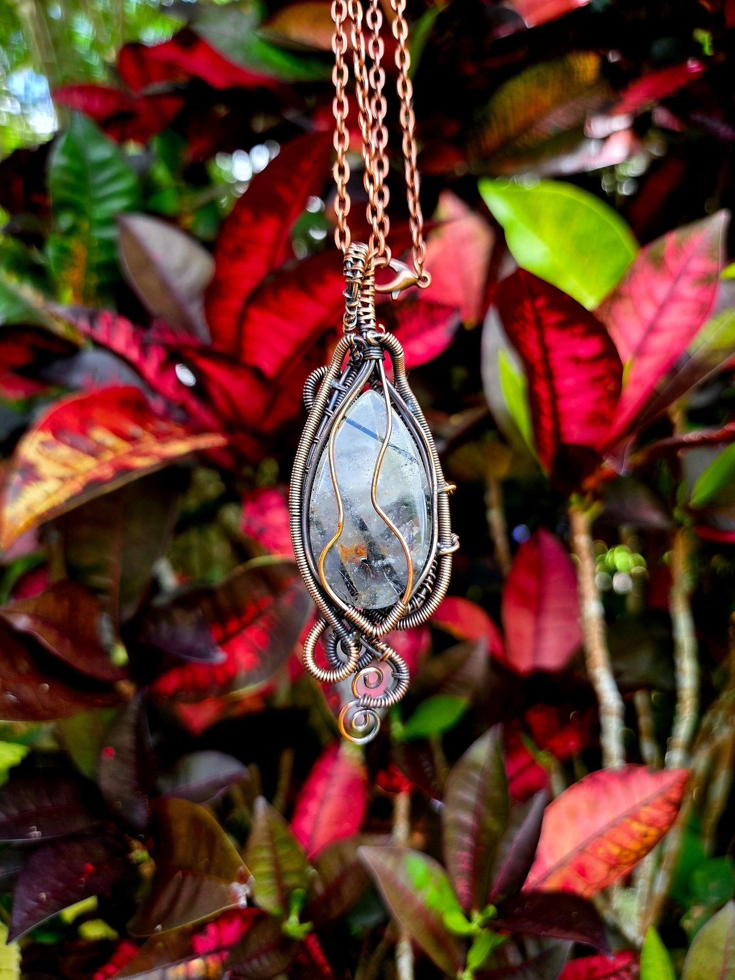 Necklace with a decorative pendant against a background of red and green leaves