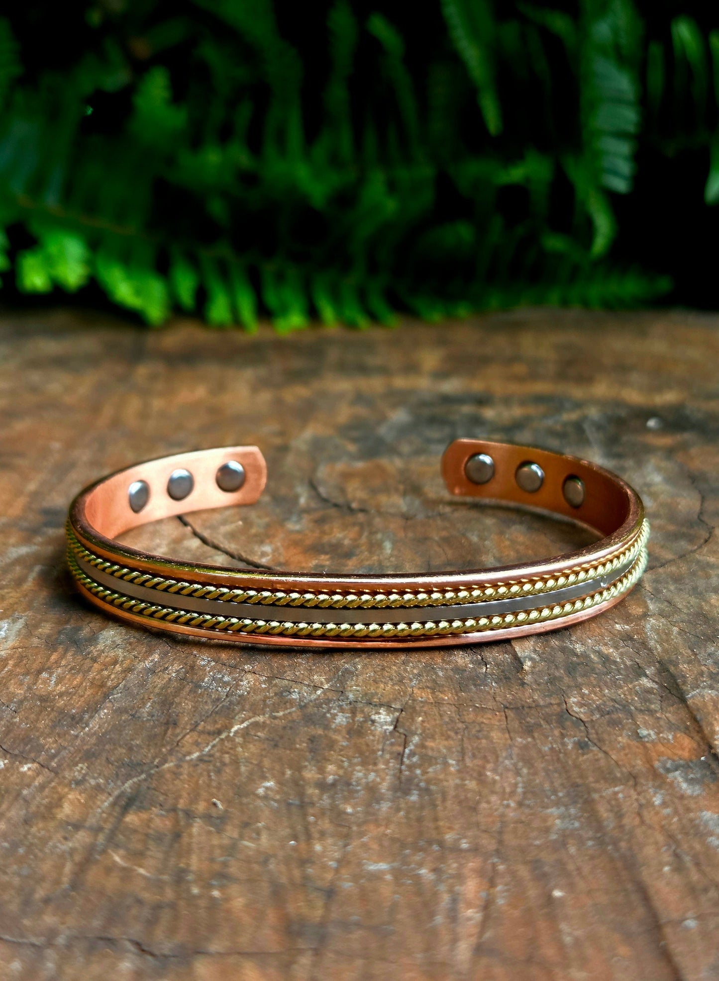 Copper bracelet with embedded stones on a wooden surface with green foliage in the background