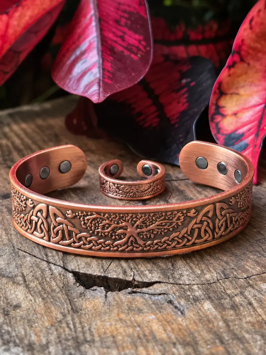 A copper engraved cuff bracelet with matching ring, displayed on a rustic wooden surface with red and black leaves in the background.