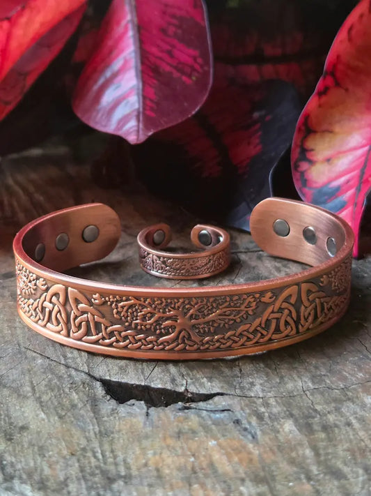 Copper bracelet with a tree of life design on a wooden surface with red leaves in the background