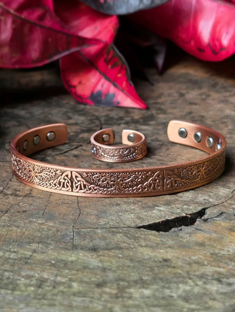 Copper bracelet and ring with intricate designs on a wooden surface with red leaves in the background