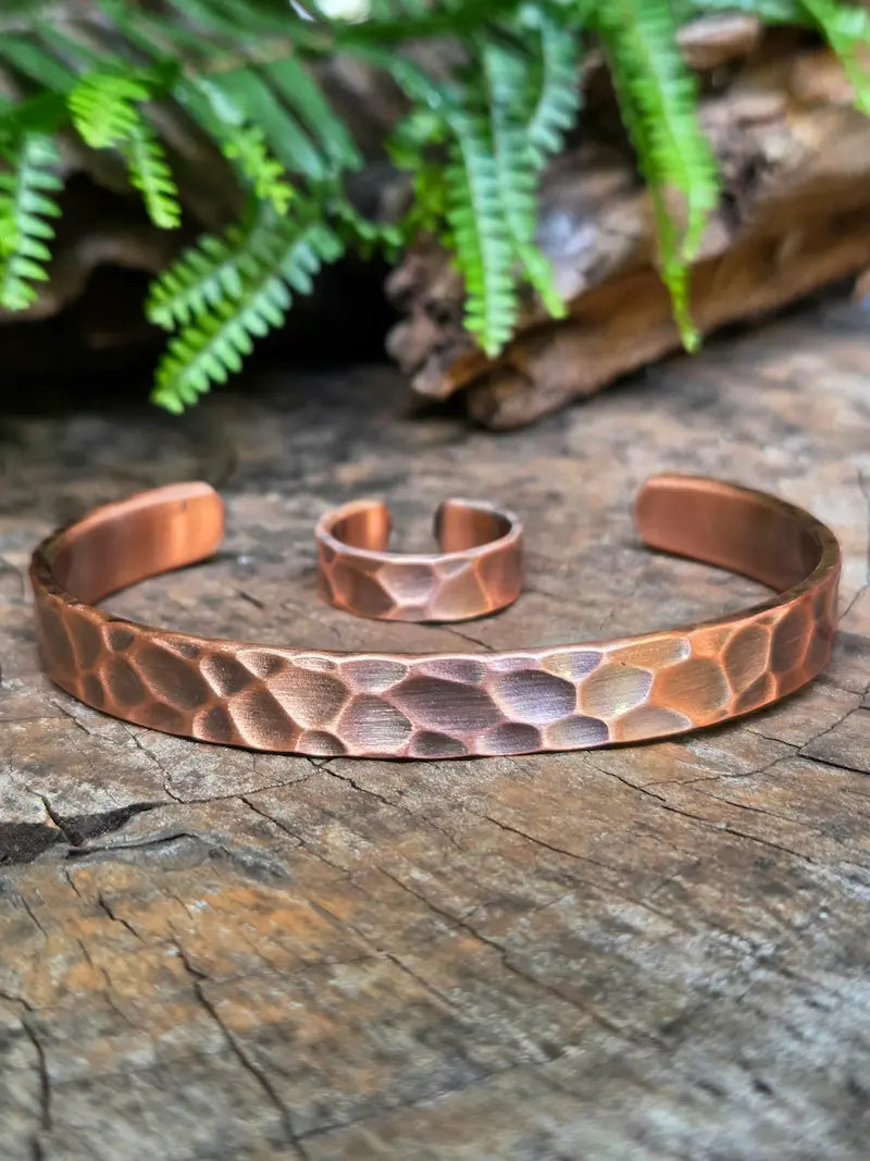 Copper bracelet and ring on a natural wooden surface with green leaves in the background 