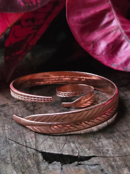 Copper bracelet and ring on a wooden surface with a red leaf in the background