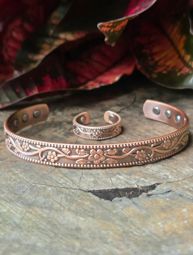 Copper bracelet and ring with floral patterns on a natural wooden surface with red leaves in the background 