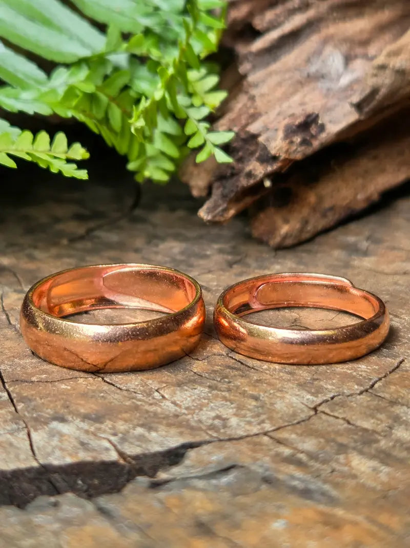Two handmade copper rings resting on a rustic wood surface with green ferns in the background.