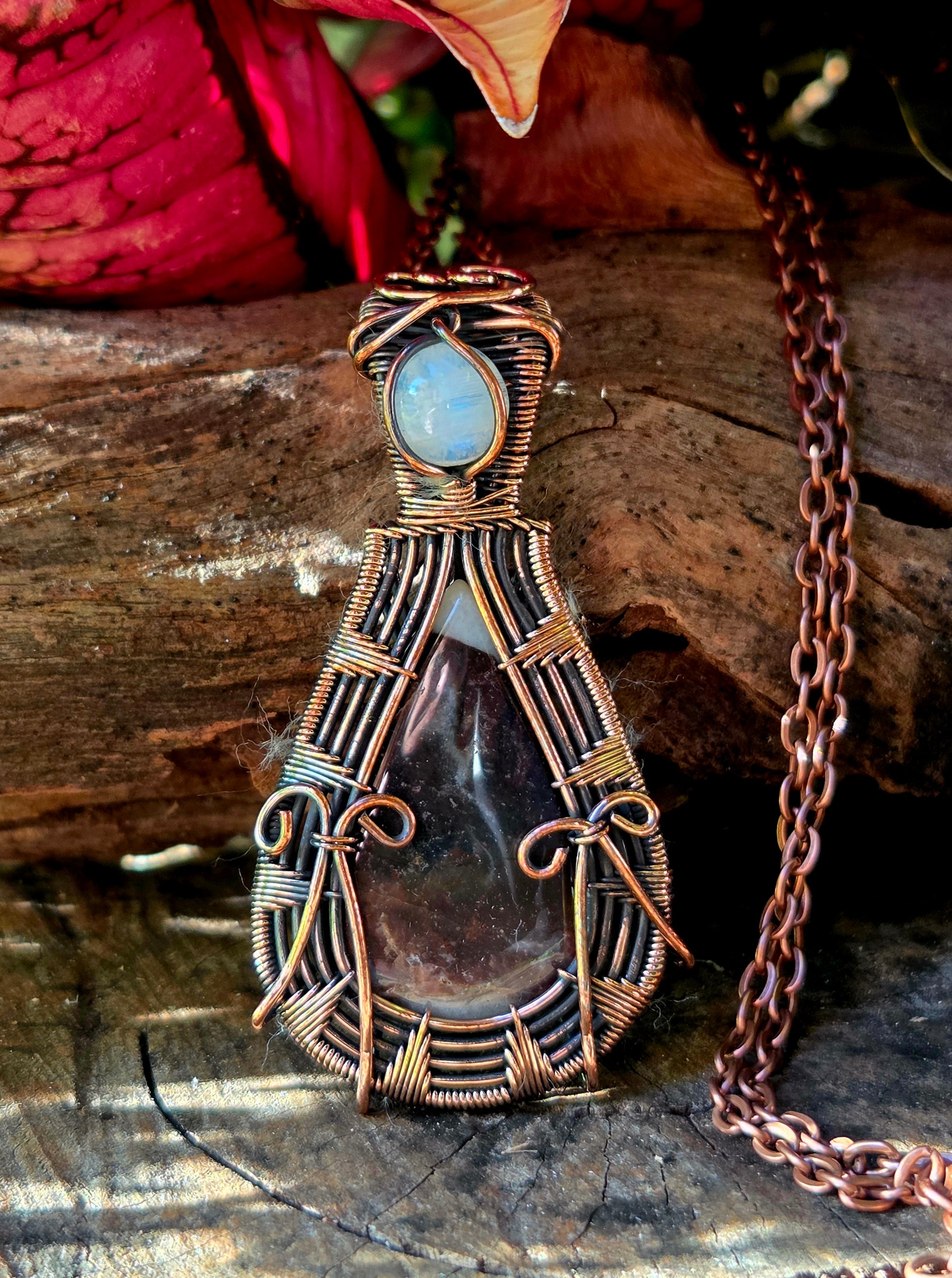 Copper pendant necklace on a natural wooden surface with leaves in the background 