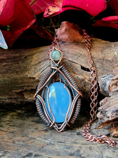 Necklace with a blue pendant on a wooden surface with red flowers in the background