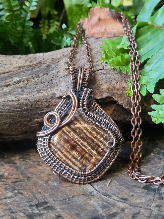 Copper wire-wrapped pendant on a chain against a natural background with greenery.
