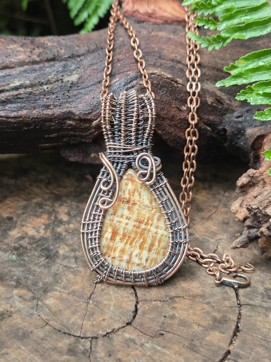 Copper necklace with a jasper pendant on a wooden surface with green leaves