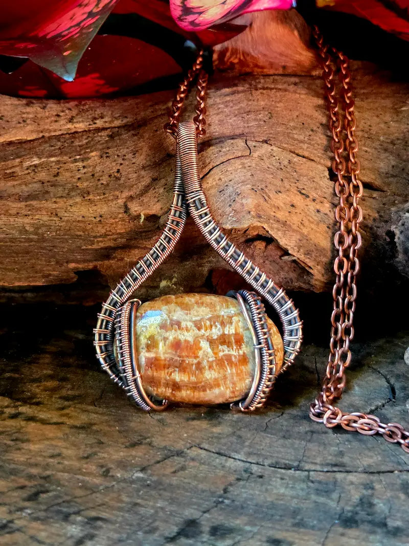 Copper-wrapped stone pendant on a wooden surface