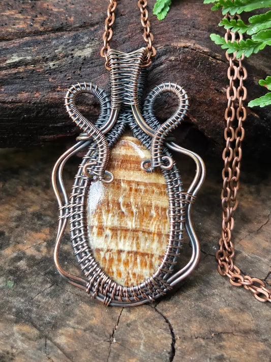 Copper necklace with a brown stone on a natural wooden surface background