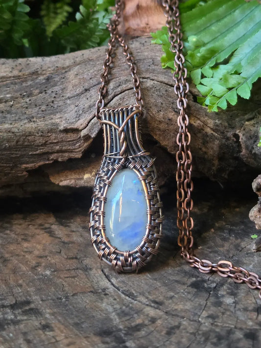 Necklace with a blue stone pendant on a wooden surface with green leaves in the background