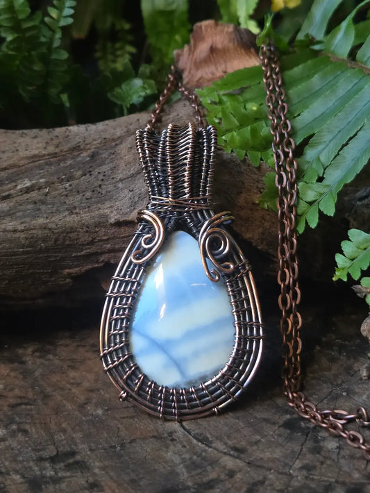 Copper necklace with a blue stone pendant on a wooden surface with green foliage