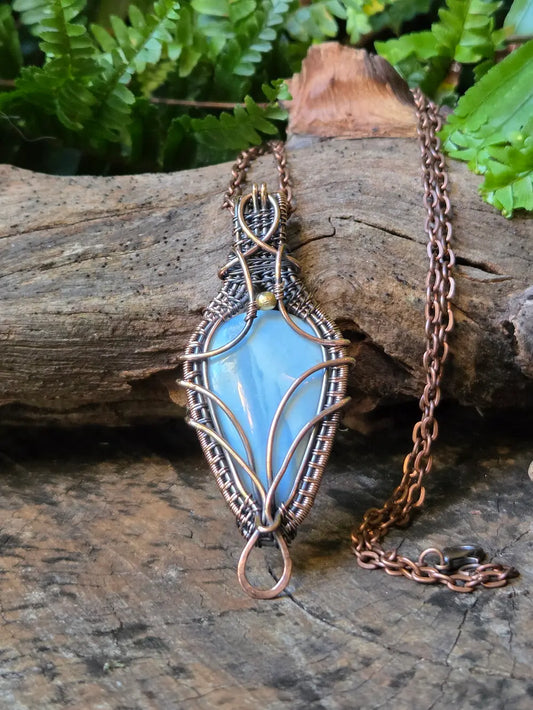Copper necklace with a blue pendant on a wooden surface with green foliage in the background