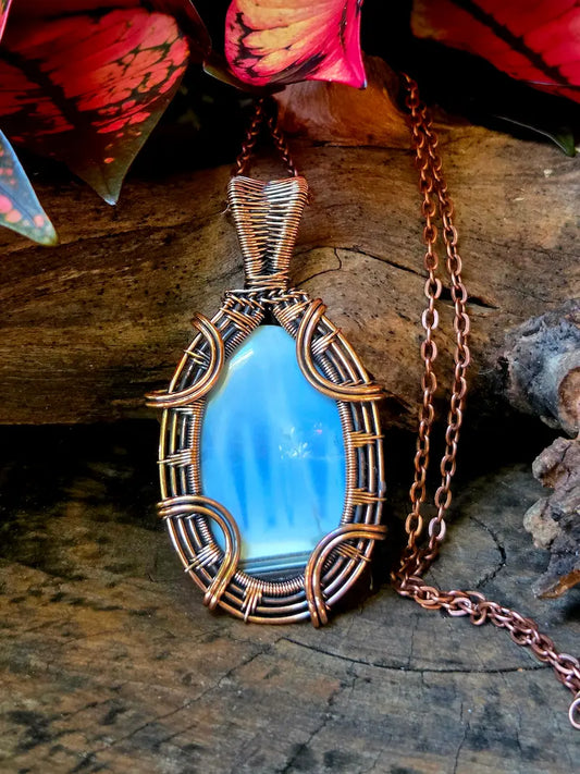 Blue pendant with copper wire wrapping on a wooden surface