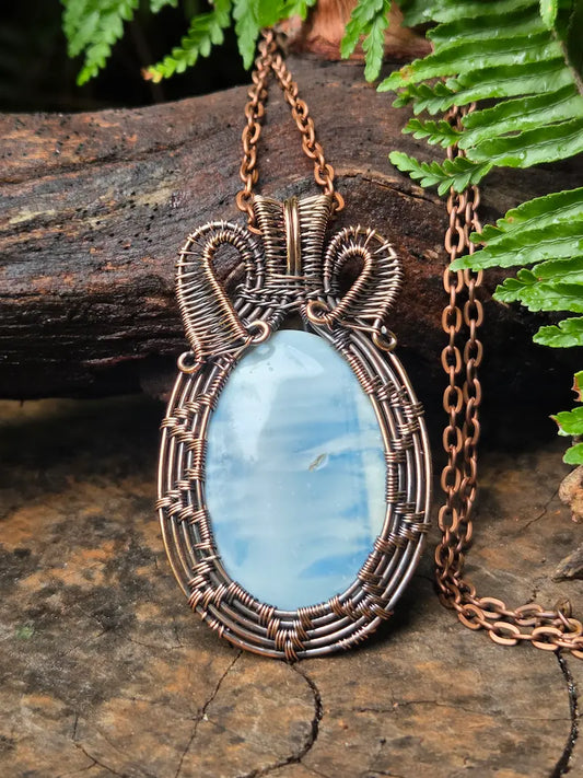 Copper-wrapped pendant with a blue stone on a wooden surface with greenery
