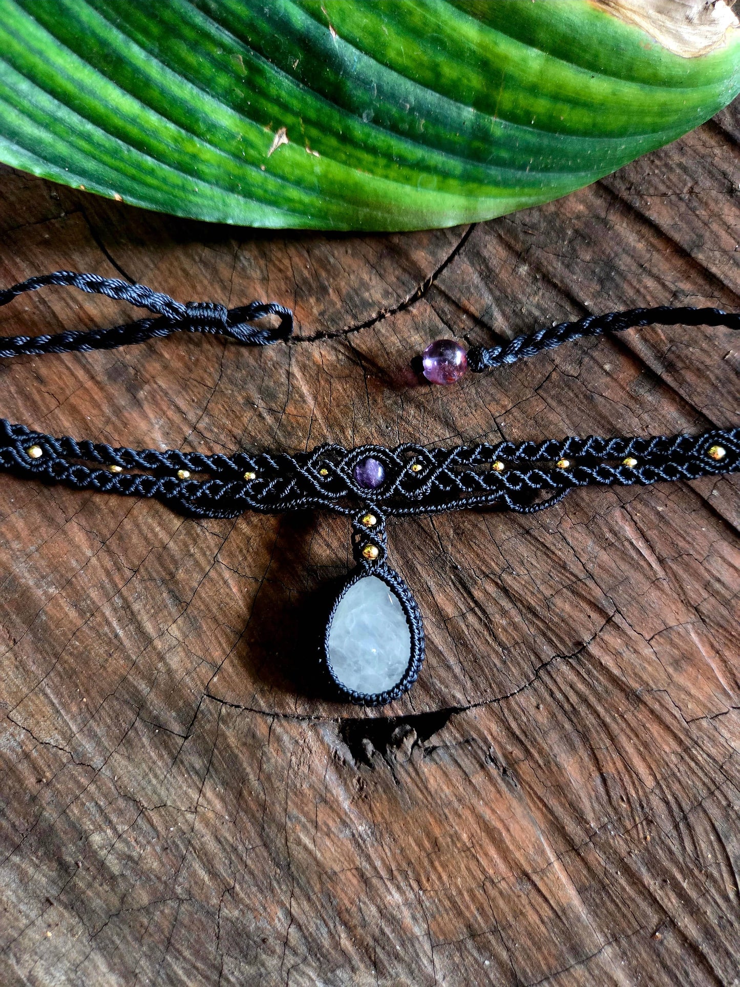 Macrame clear quartz necklace on a wooden surface with green leaves in the background