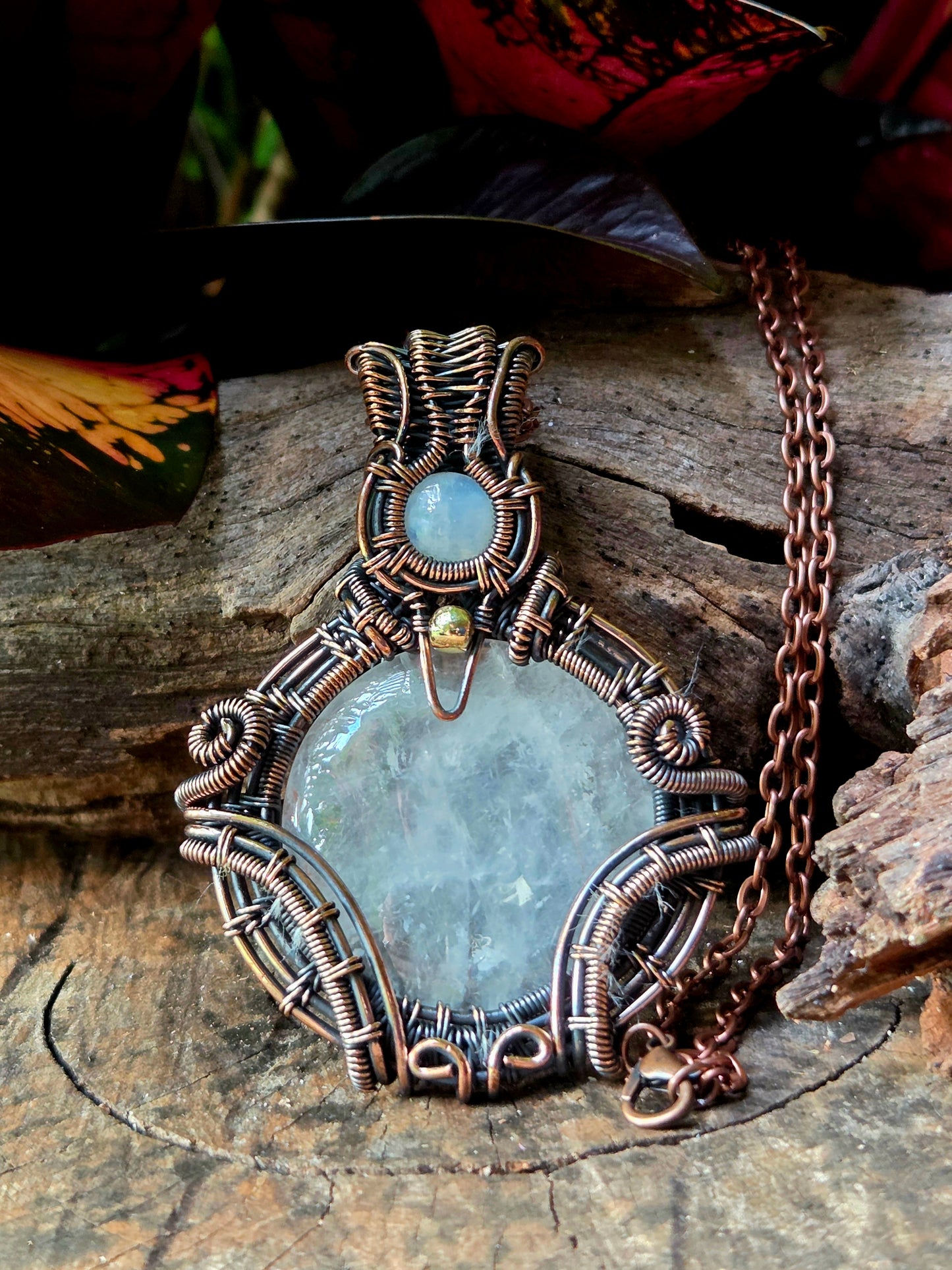 Clear Quartz Copper necklace on a natural wooden surface with red leaves in the background 
