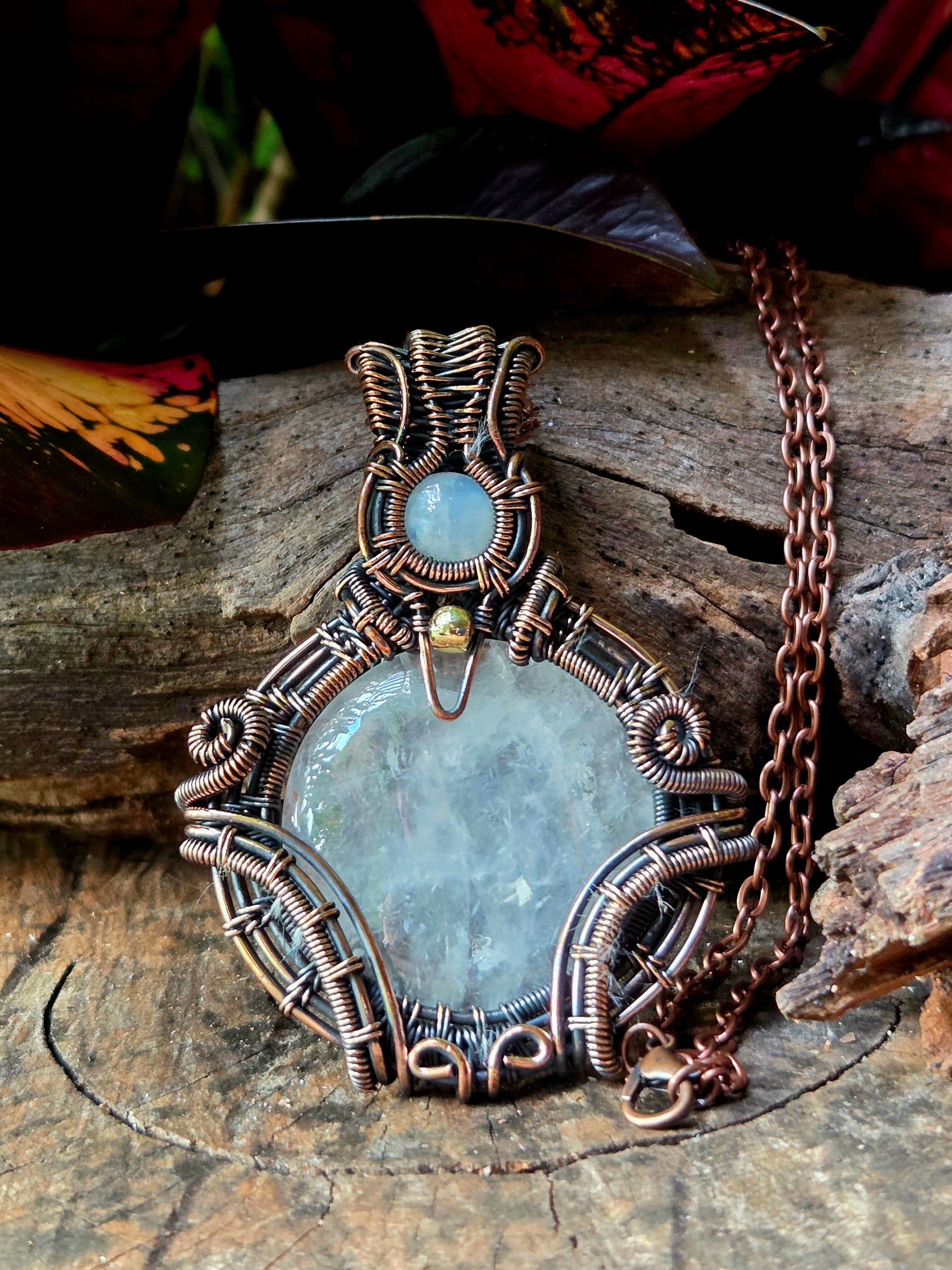 Clear Quartz Copper necklace on a natural wooden surface with red leaves in the background 