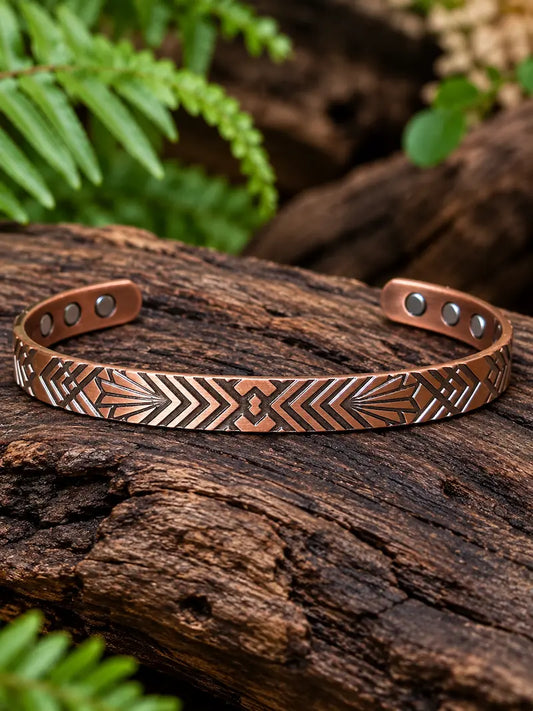 Copper Bracelet with a geometric pattern resting on a natural wooden surface with green ferns in the background 