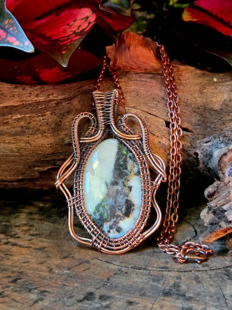Copper-wrapped pendant with a natural stone on a wooden surface