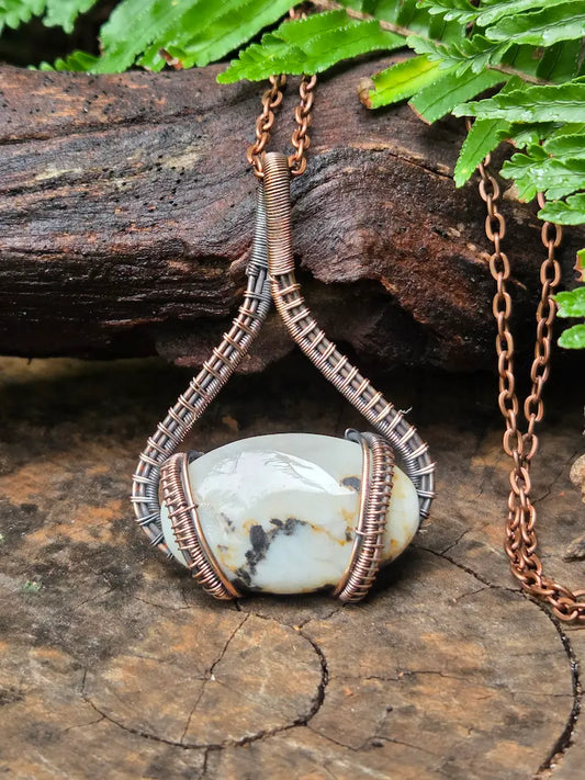 Copper necklace with a stone pendant on a wooden surface with greenery