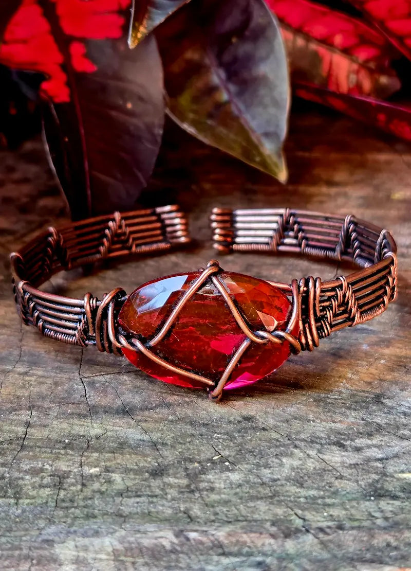 Copper bracelet with a red gemstone on a wooden surface