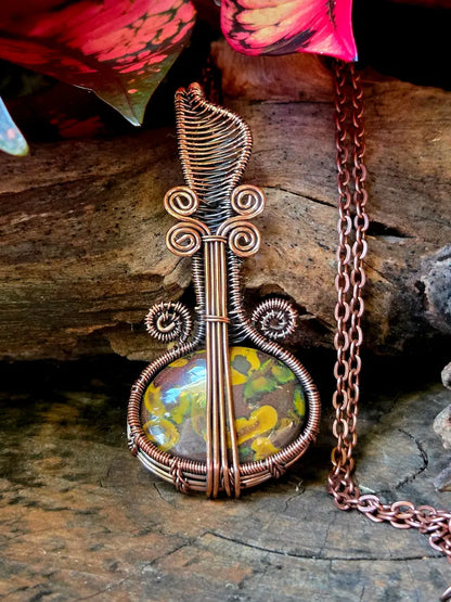 Copper wire-wrapped pendant with a colorful stone on a wooden surface