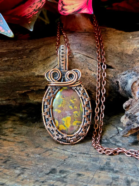 Copper wire-wrapped pendant with a colorful stone on a wooden surface