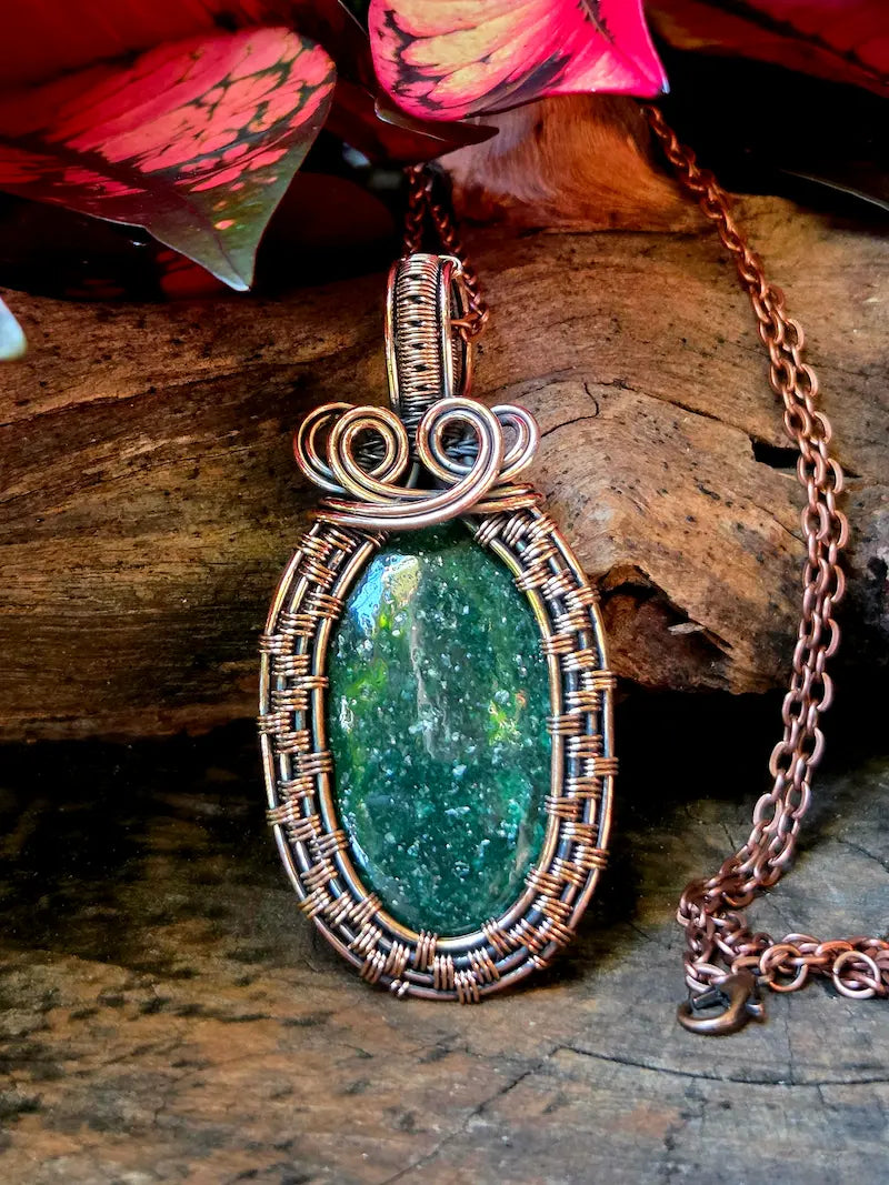 Green stone pendant with copper wire wrapping on a wooden surface