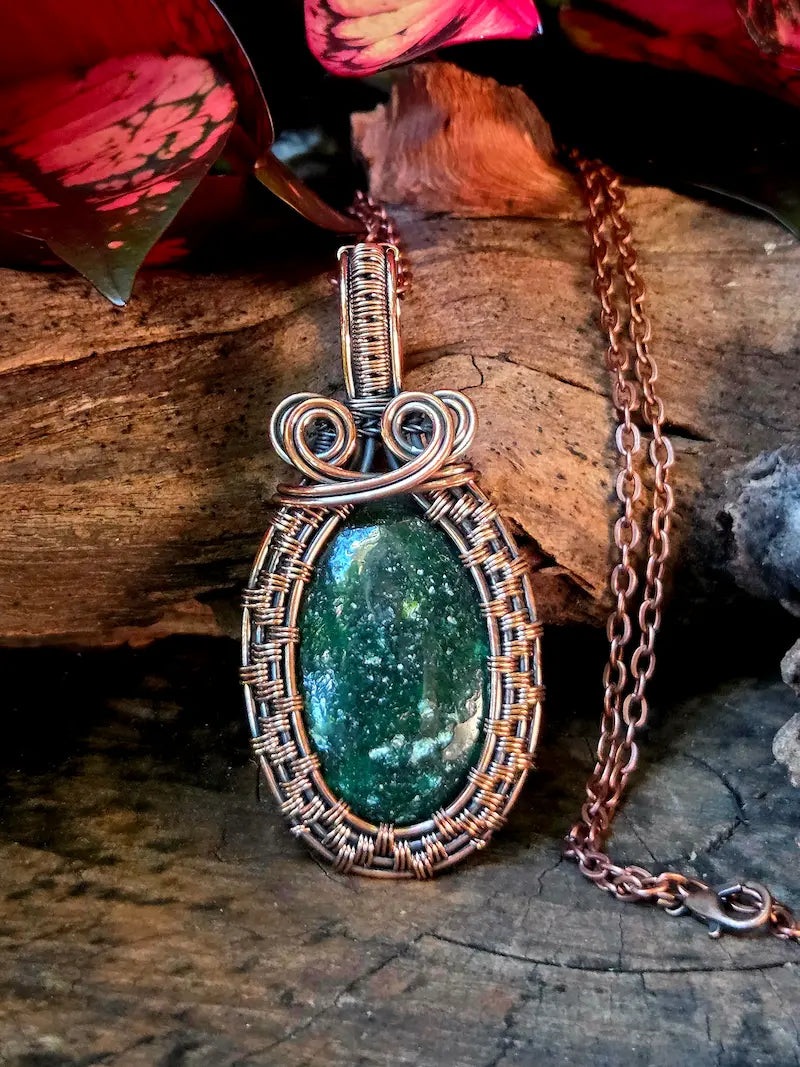 Green gemstone pendant with copper wire wrapping on a wooden surface