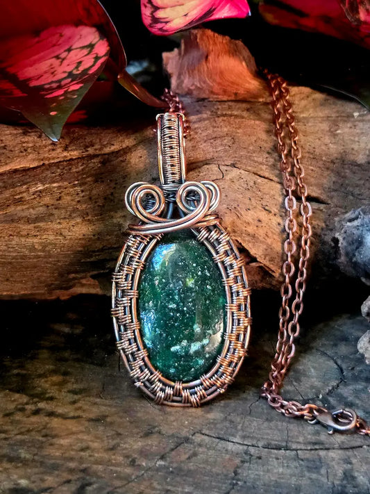 Green gemstone pendant with copper wire wrapping on a wooden surface