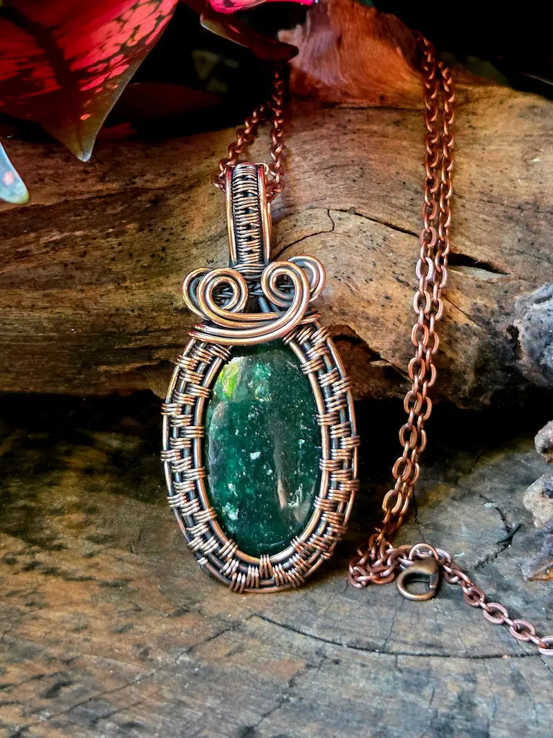 Green stone pendant with copper wire wrapping on a wooden surface