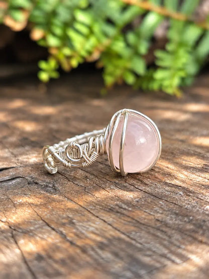 Handmade silver-coloured copper wire wrapped ring on a natural wooden surface with green ferns in the background 