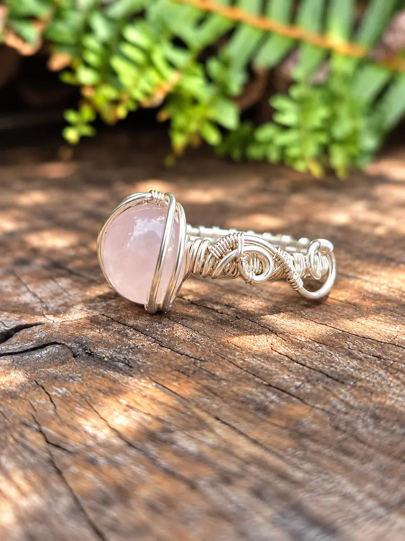 Handmade silver-coloured copper wire wrapped ring on a natural wooden surface with green ferns in the background 