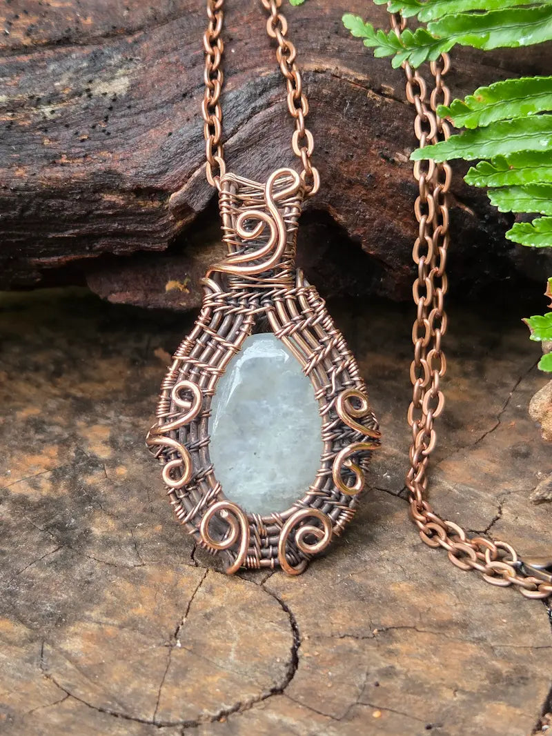 Copper necklace with moonstone pendant on a natural wooden background 