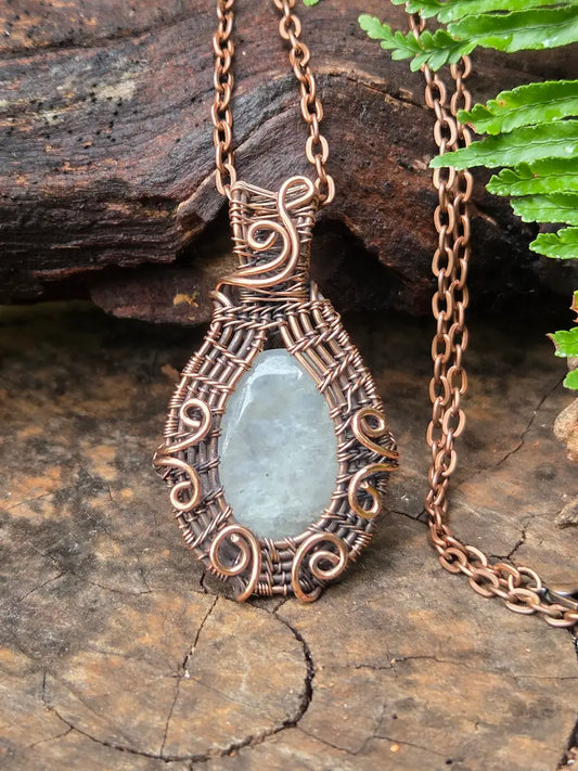 Copper necklace with moonstone pendant on a natural wooden background 