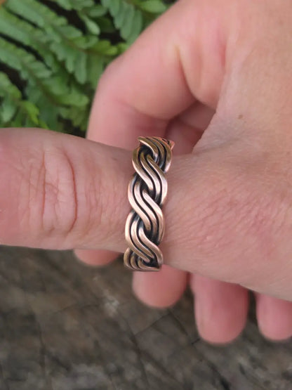 A close-up of a hand wearing a copper twisted style ring with a two-tone finish of rose gold and dark bronze.