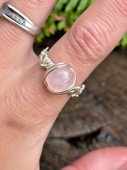 Handmade silver-coloured copper wire wrapped ring on a hand with a natural wooden background and green ferns