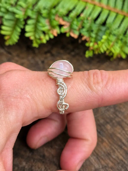 Handmade silver-coloured copper wire wrapped ring on a hand with a natural wooden background and green ferns