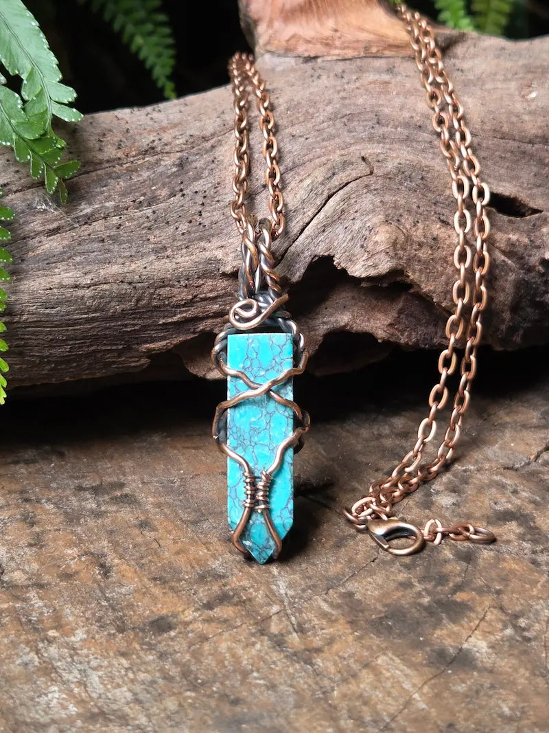 Handmade coppet wire wrapped pendant necklace on a natural wooden surface with green leaves in the background 