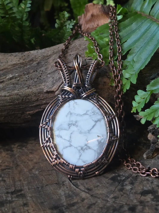 Copper necklace with a pendant featuring a white stone on a wooden surface with green leaves.
