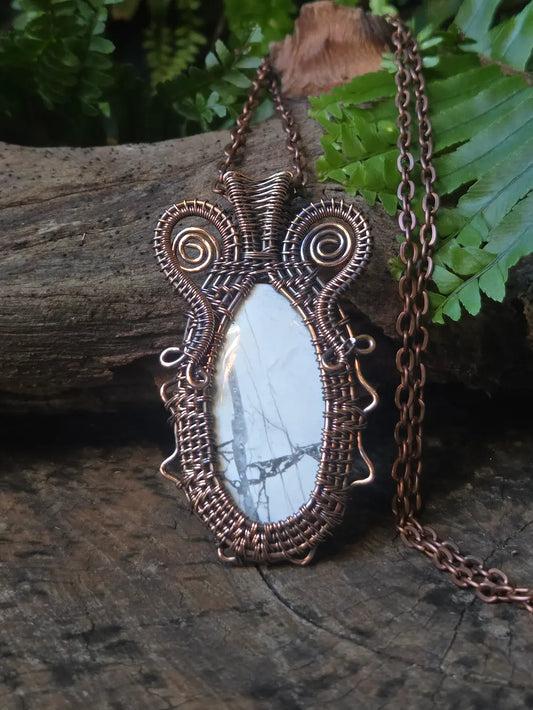 Copper pendant on a wooden log with ferns in the background