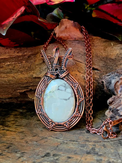 Copper-wrapped necklace with a howlite stone on a wooden surface with red flowers in the background