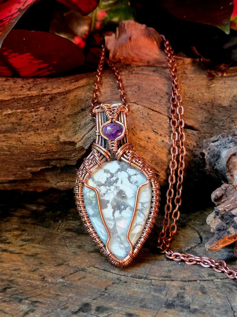 Copper necklace with a howlite pendant placed on a natural wooden surface.