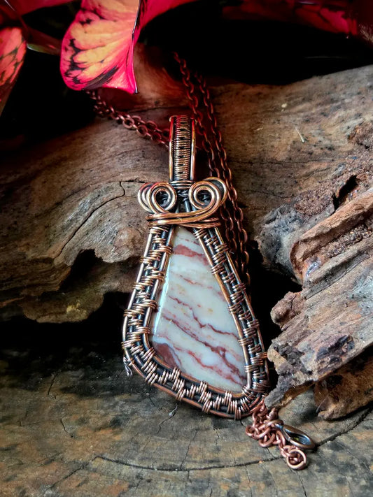 Copper wire wrap necklace with a jasper stone pendant on a wooden surface